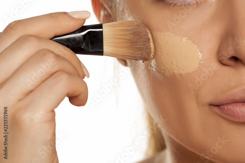 Fototapete Young woman applying liquid foundation with brush on white background