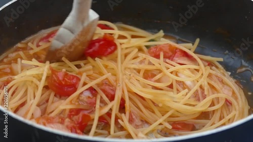 Mixing Spaghetti with tomato and basil with a wooden spoon in a large frying pan. photo