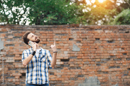 Attractive young bearded hipster with mobile phone pointing up.