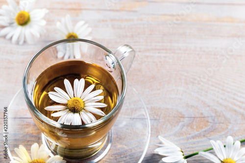 Cup of medicinal chamomile tea and flowers of chamomile on a wooden background with copy space.