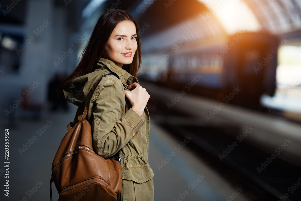 Happy young woman waitng train on the railway station platform. Woman travel with the train.
