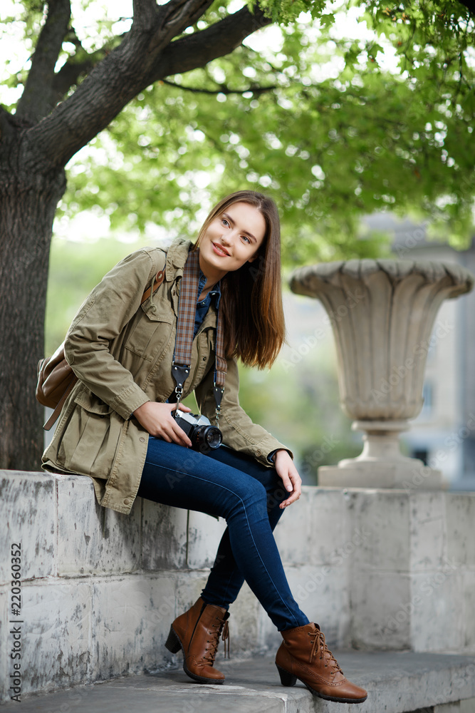 Young beautiful woman sitting on bench in park. Traveler with vintage camera.
