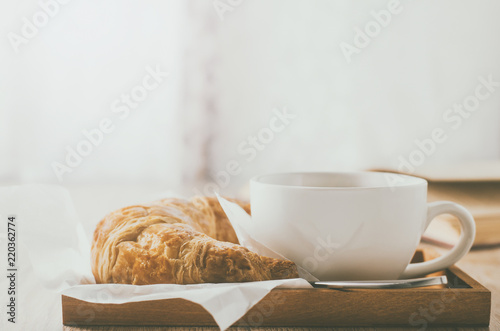 Close up of coffee cup with croissant on wooden table with vintage tone