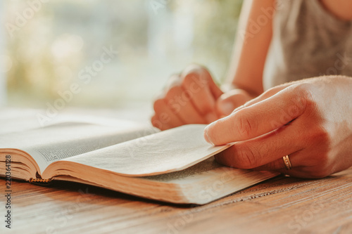 Christian worship and praise. Hands of a young woman on an open Bible in the early morning