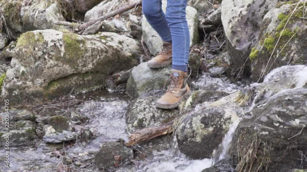 Woman with boots and jeans carefully crossing over a small stream from a waterfall_slomo Woman with boots and jeans carefully crossing over a small stream from a waterfall_slomo
