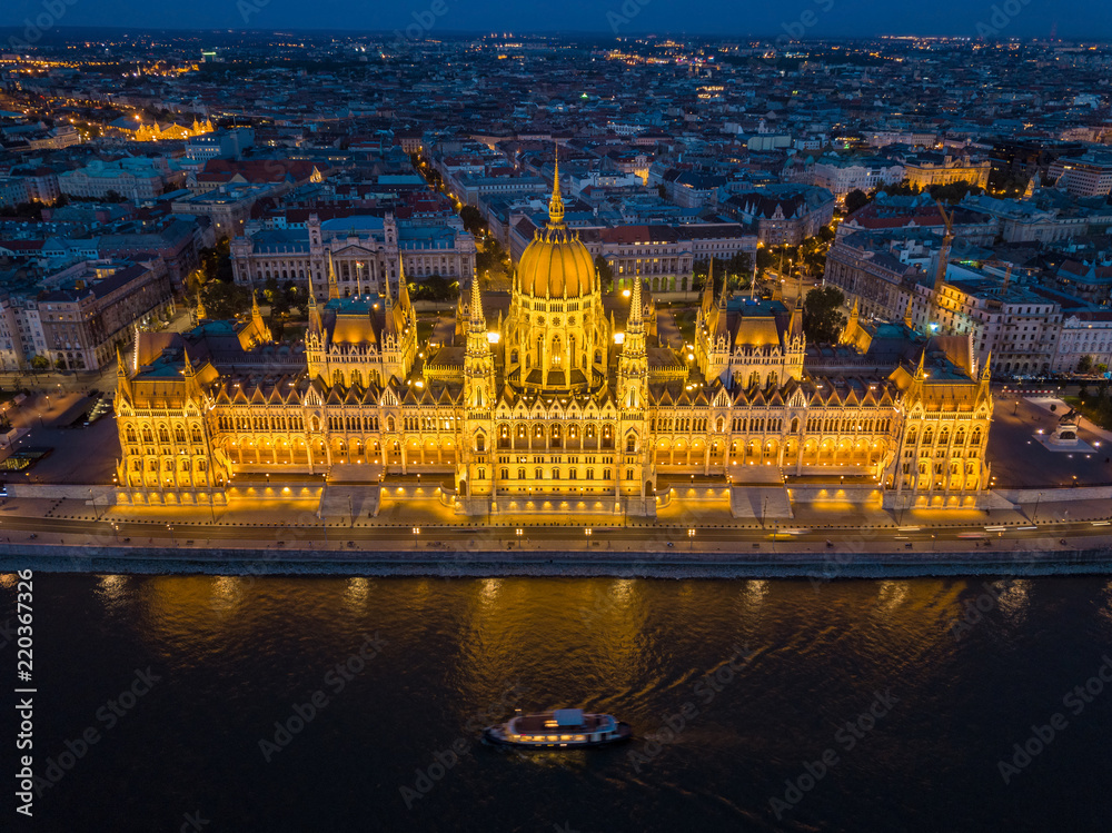 Budapest, Hungary - Aerial blue hour view of the illuminated Parliament of Hungary with sightseeing boat on River Danube and skyline of Budapest at background