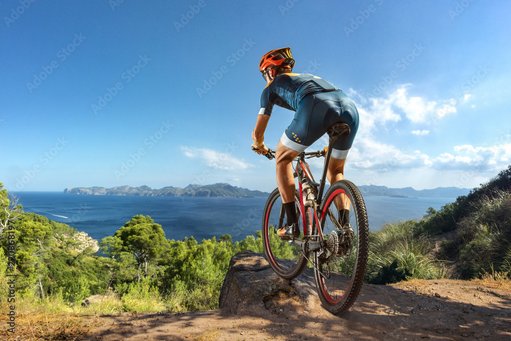 Fototapeta premium Cross-Country biker on stone trail near the lake. Male cyclist rides the rock