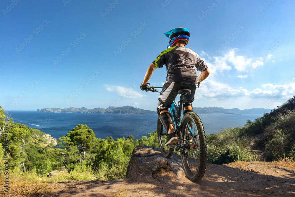 Mountain biker on forest trail near the lake. Male cyclist rides the rock