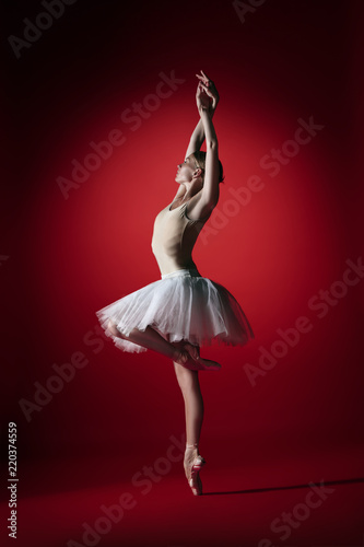 Young graceful female ballet dancer or classic ballerina dancing at red studio. Caucasian model on pointe shoes