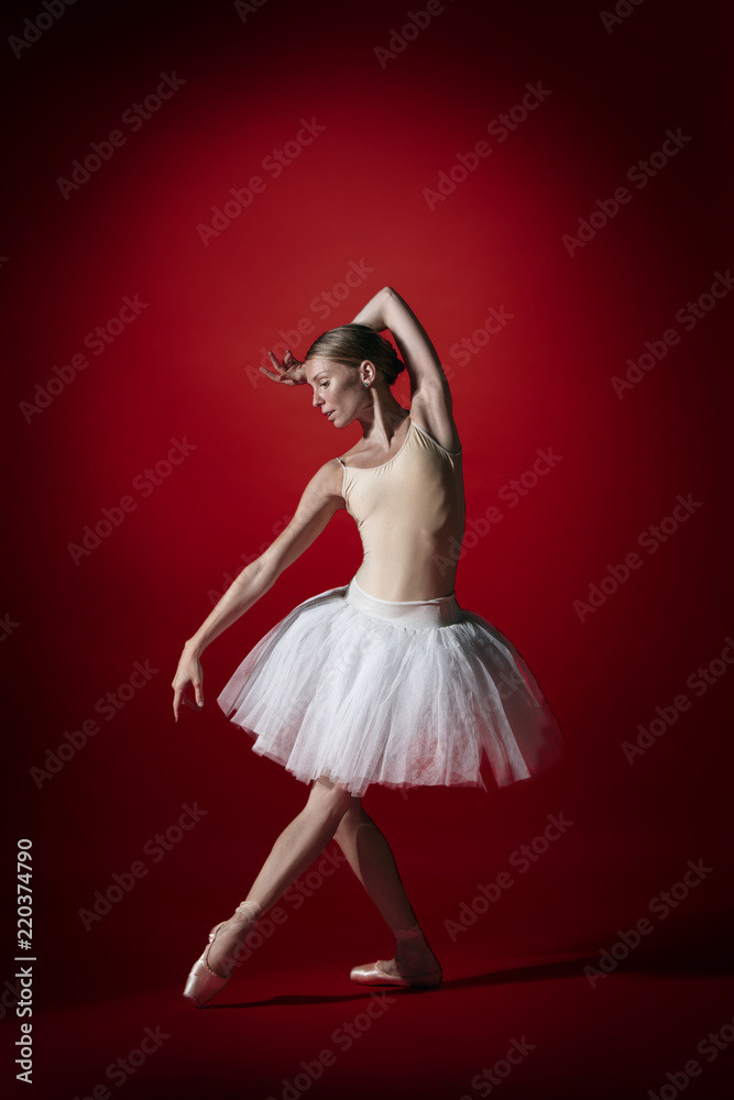 Fototapeta premium Young graceful female ballet dancer or classic ballerina dancing at red studio. Caucasian model on pointe shoes