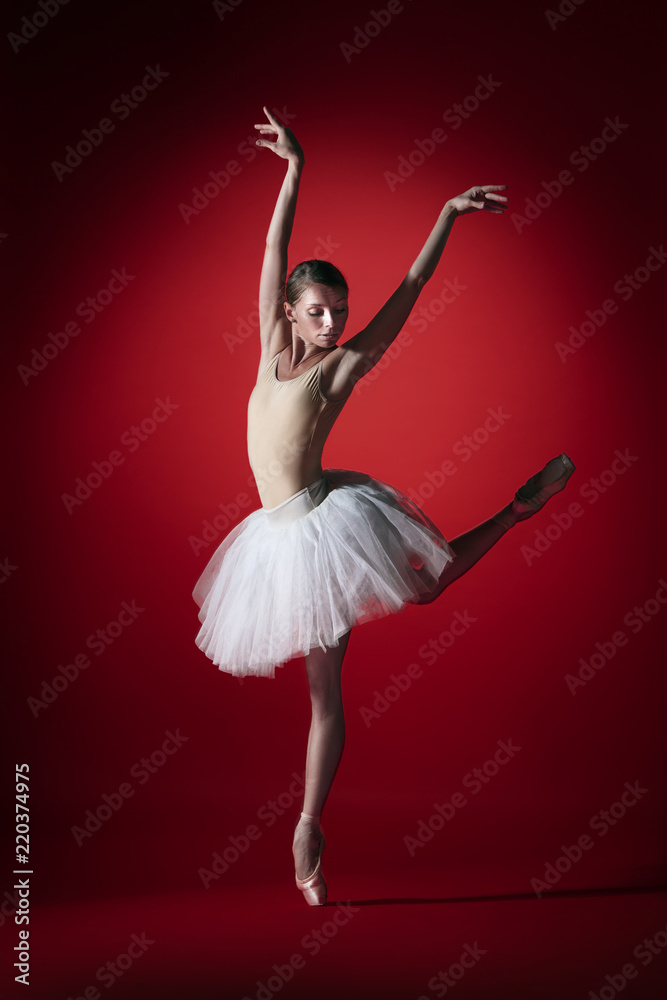 Fototapeta premium Young graceful female ballet dancer or classic ballerina dancing at red studio. Caucasian model on pointe shoes