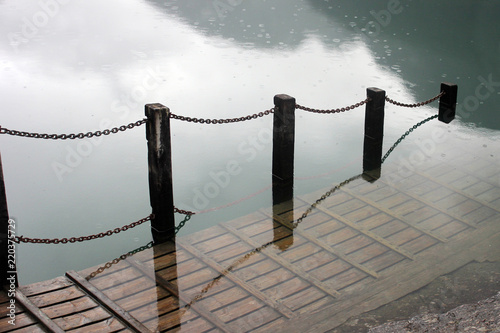 Waterlogged wooden platform with metal chain railing on a river bank photo