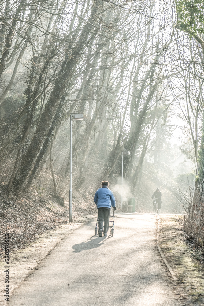 Alter Mann von hinten mit Rollator bei Kälte in Hohlweg