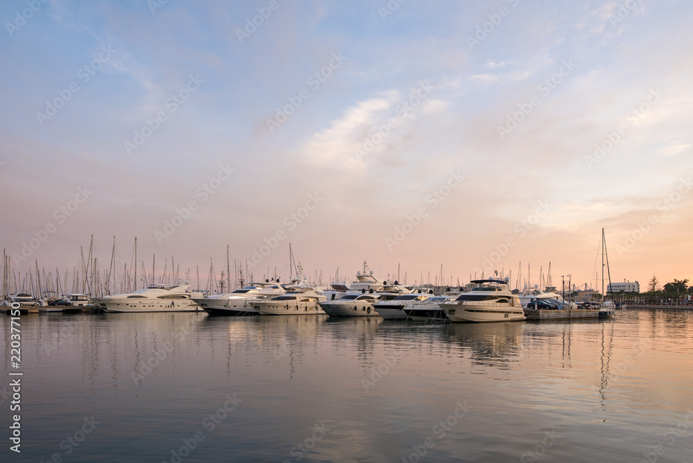 Fototapeta premium Beautiful port of Alicante, Spain at Mediterranean sea. Luxury yachts, ships, ferries and fishing boats sailing and standing in rows in harbor. Rich people traveling around the world. Sunset evening
