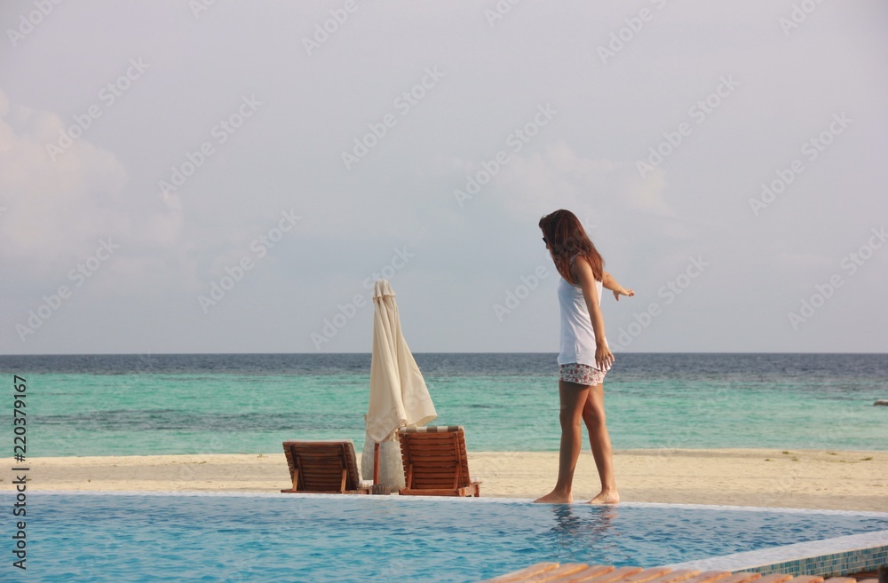 Girl walking on the edge of the swimming pool on Maafushivaru beach, Maldives