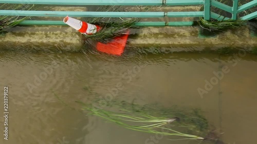 Orange cone on a flooded sidewalk as debris floats by next to the Yahara River in Madison, WI. photo