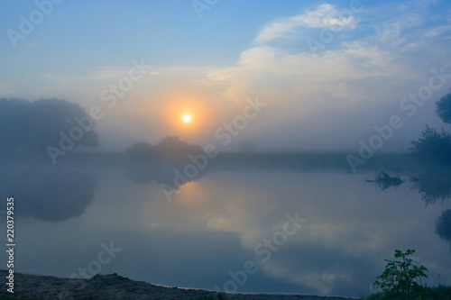 Orange sunrise over the river surface with fog in summer morning. River landscape at sunrise