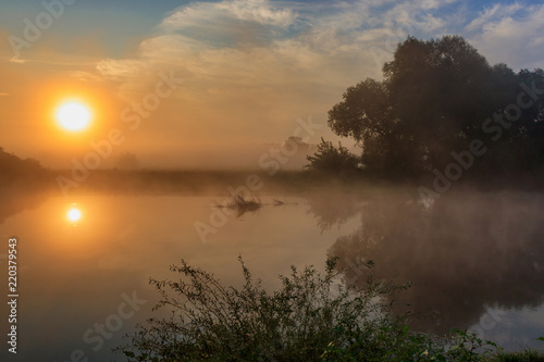 Water surface of river at sunrise with reflection of orange sun. River landscape in sunny summer morning