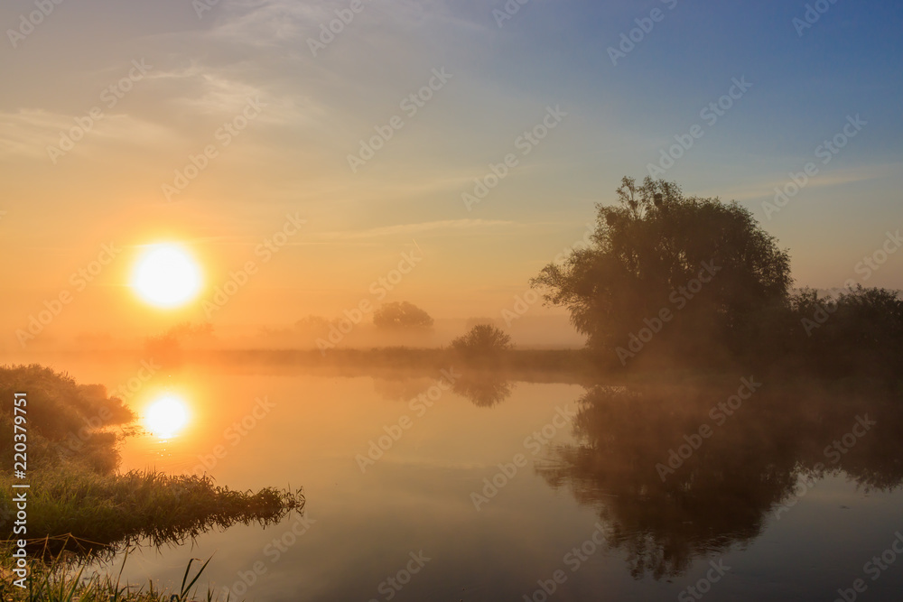 Orange sunrise over the river in fog. River landscape in summer morning
