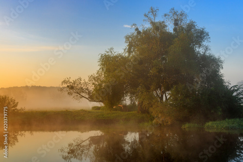 Orange sunrise with fog over river surface against blue sky. River landscape in summer morning