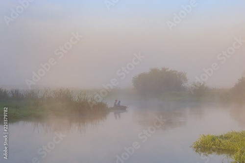Two young men catching fish from an inflatable boat on the river in early morning. River landscape