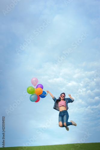 Asain woman holding colorful balloons and jumping in to blue sky and white clouds background.