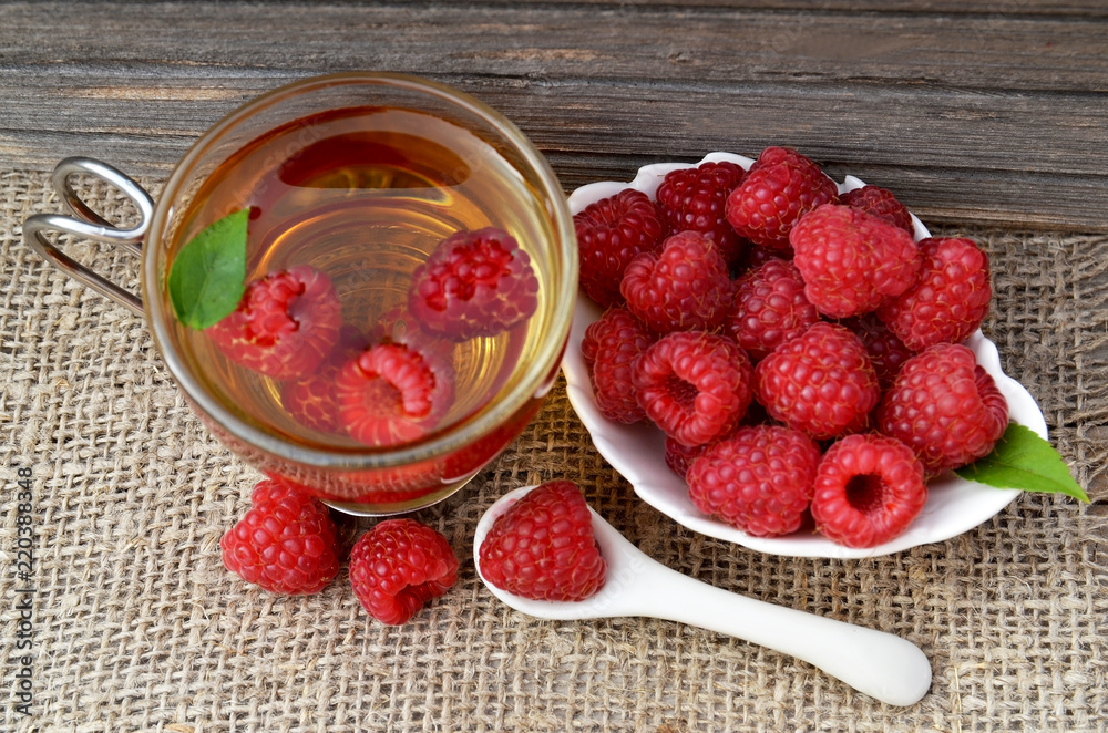 Raspberry tea with fresh picked berries in a glass transparent cup on old wooden table.Natural herbal beverage.Top view. Raspberry tea with fresh picked berries in a glass transparent cup on old wooden table.Natural herbal beverage.Top view.