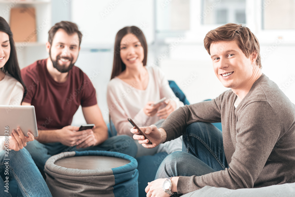 My device. Nice handsome man holding his smartphone while sitting together with his friends