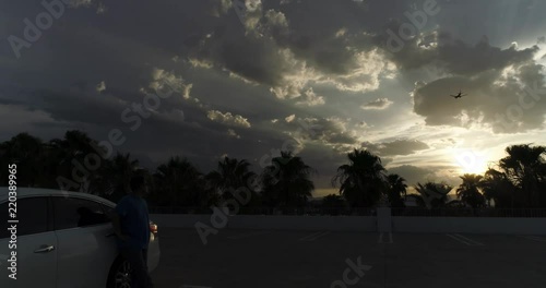 Man Standing Next To Car Watching Airplane Flying Towards Airport In Nevada At Sunset