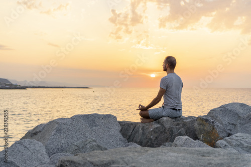 Spain. Man meditating during sunrise on rocky beach