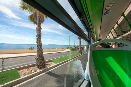 Fototapeta Naklejka Na Ścianę i Meble -  View of palm trees and seaside from public transportation bus. People are going to vacation, enjoying beach holidays. Sunny summer day, tropical weather.  
