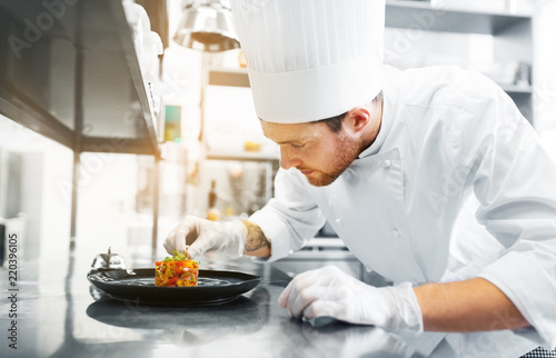 food cooking, profession and people concept - happy male chef cook serving and garnishing stewed vegetables on plate at restaurant kitchen photo