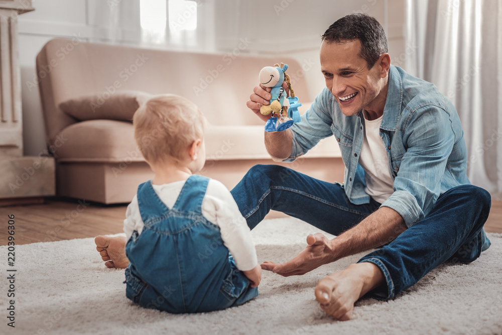 Fototapeta premium So much fun. Delighted nice man holding a toy while playing with his baby