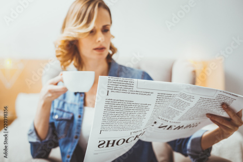 Serious morning. Exciting woman holding newspaper and reading news
