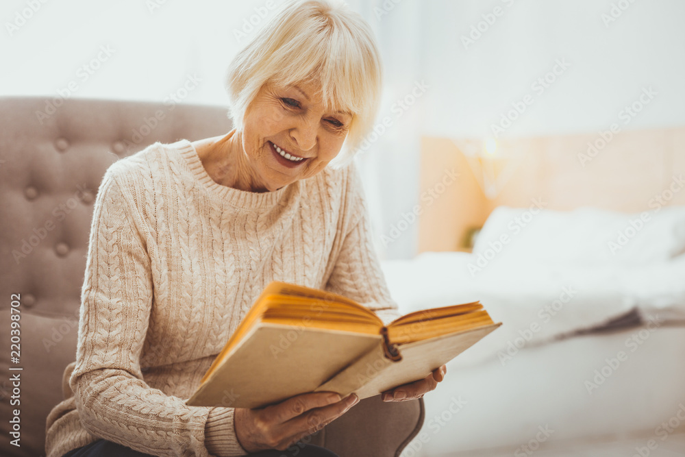 Interesting story. Delighted senior woman expressing positivity while staring at her book