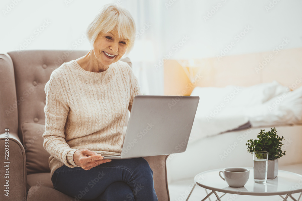 Online conversation. Amazing pensioner bowing head while holding laptop on knees Online conversation. Amazing pensioner bowing head while holding laptop on knees