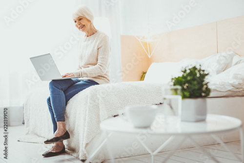 Happy femininity. Happy mature woman holding laptop on knees while checking email