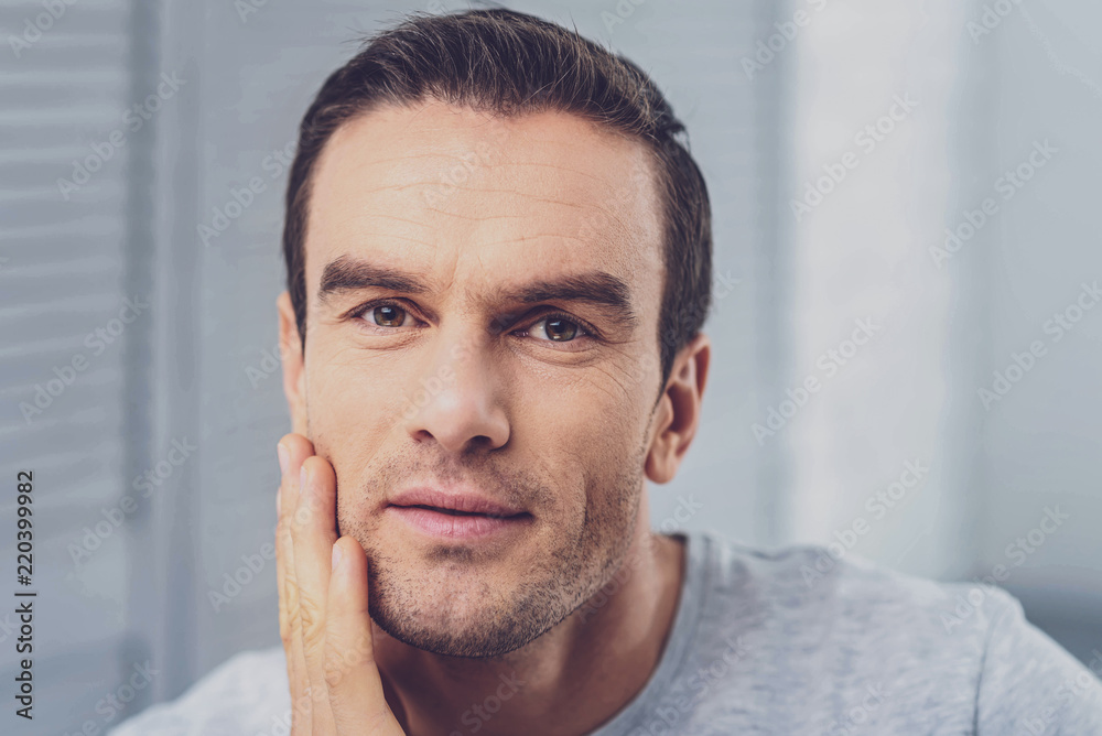 Facial wrinkles. Pleasant handsome man with facial wrinkles feeling wonderful while standing in light room at home Facial wrinkles. Pleasant handsome man with facial wrinkles feeling wonderful while standing in light room at home