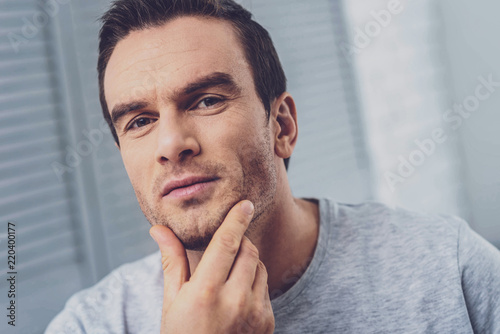 Bristle chin. Pleasant handsome mature man touching his bristle chin while feeling thoughtful realizing some surprising facts