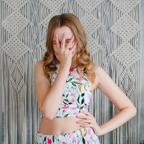 Portrait of a cute young woman doing facepalm on background of macrame wall. photo