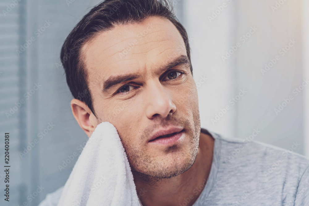 Fototapeta premium In the bathroom. Handsome mature man toweling off his face while getting ready for work in the bathroom