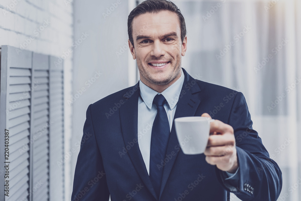 Cheerfulness. Portrait of positive delighted businessman spending leisure time with a cup of invigorating fragrant espresso