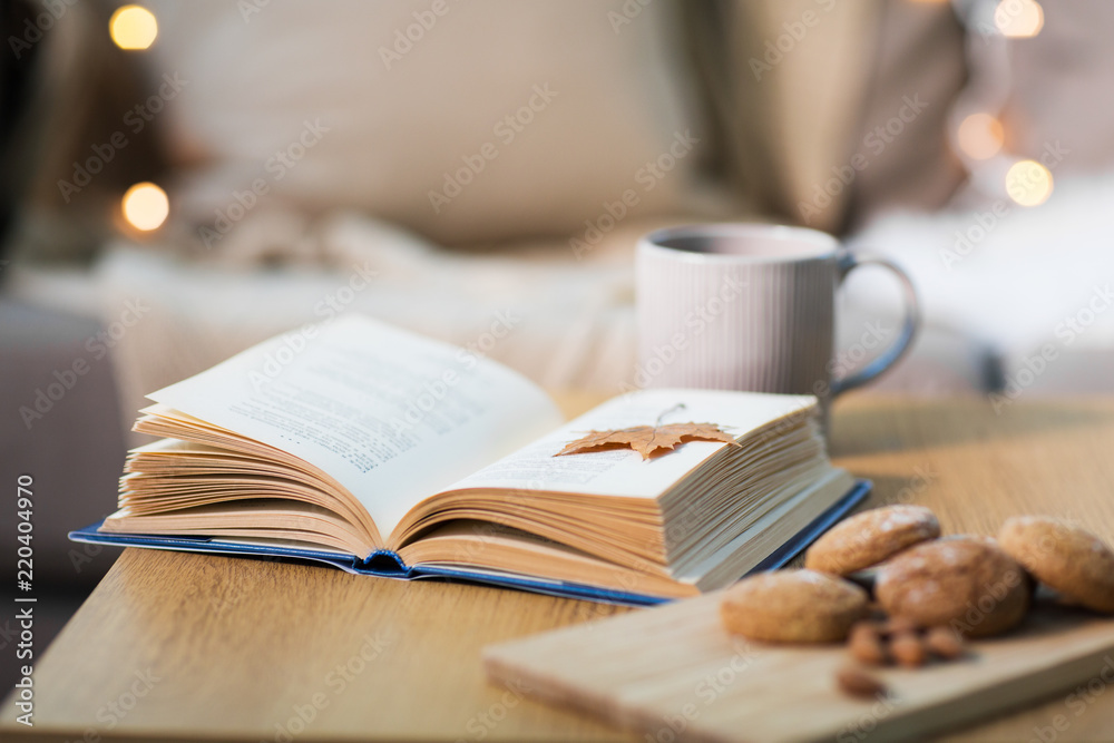 hygge and cozy home concept - book with autumn leaf, cup of tea and oatmeal cookies on wooden table hygge and cozy home concept - book with autumn leaf, cup of tea and oatmeal cookies on wooden table