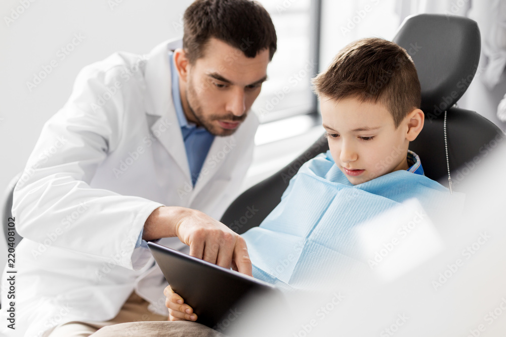medicine, dentistry and healthcare concept - male dentist showing tablet pc computer to kid patient at dental clinic medicine, dentistry and healthcare concept - male dentist showing tablet pc computer to kid patient at dental clinic
