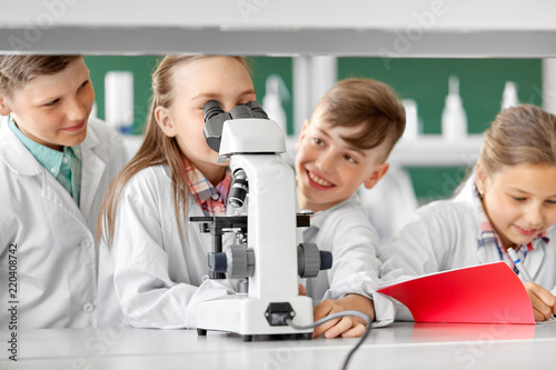 education, science and children concept - kids or students with microscope studying biology at school laboratory