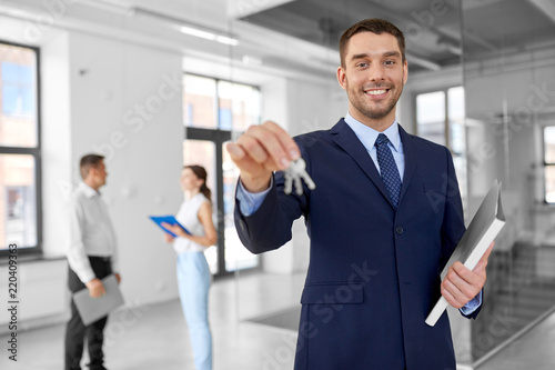 real estate business, sale and people concept - smiling realtor with keys and folder and customers at new office photo