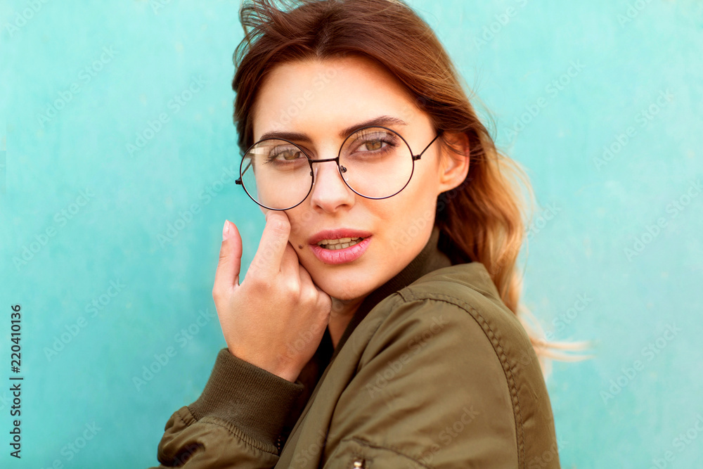 fashion girl in round glasses stands posing near a turquoise wall fashion girl in round glasses stands posing near a turquoise wall