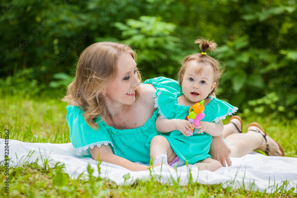 Young mother and daughter in identical dresses lay on the grass Young mother and daughter in identical dresses lay on the grass