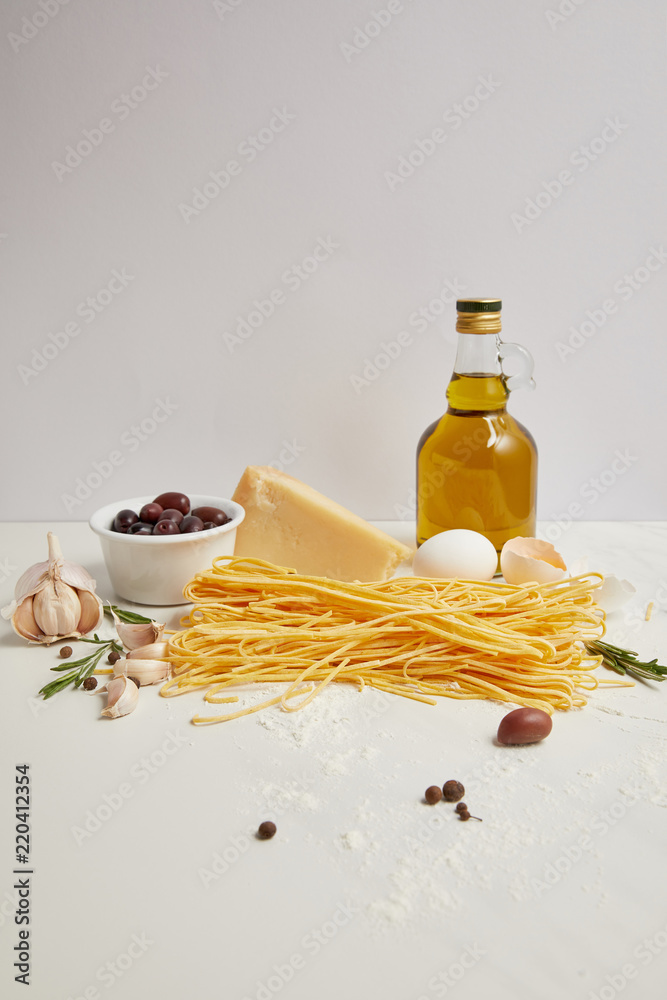 close up view of olive oil, uncooked macaroni, rosemary and cheese for cooking pasta on white tabletop close up view of olive oil, uncooked macaroni, rosemary and cheese for cooking pasta on white tabletop