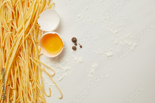 top view of uncooked macaroni, raw chicken egg and flour for cooking pasta arranged on white surface